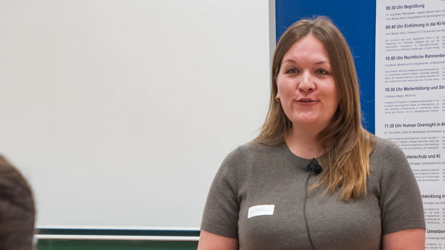 Eine Frau steht vor einer blauen Pinnwand und spricht zu einem Publikum
